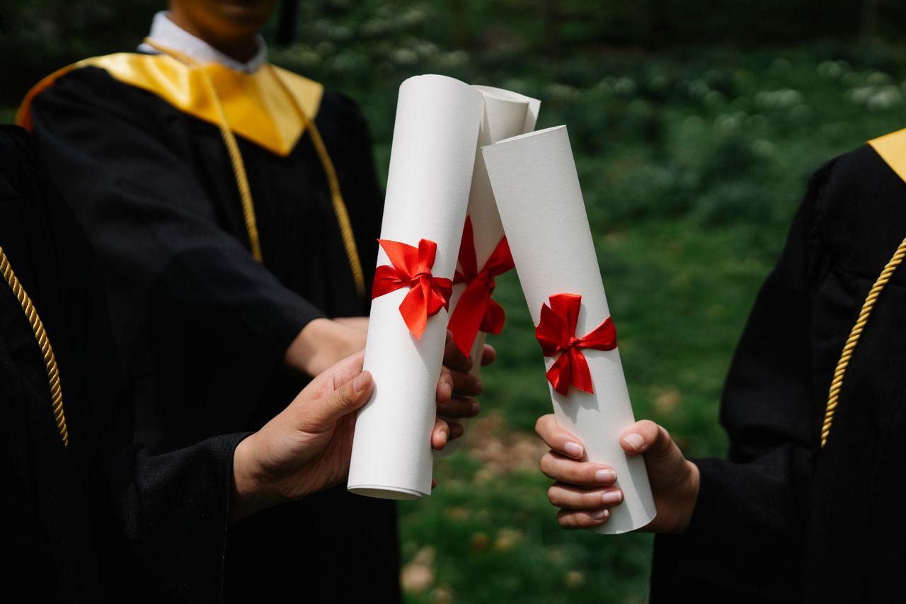 The Art of Drawing Readers In: Your attractive post title goes here Group of graduates holding diplomas with red ribbons during a ceremony outdoors.